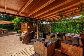 Un patio al aire libre con mobiliario de mimbre, una pérgola de madera y un exuberante fondo verde.