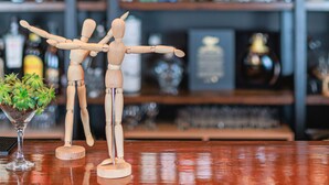 A bar with wooden figures, shelves of liquor bottles, and hanging pendant lights. - La Posada de la Gula (Jarandilla de la Vera)