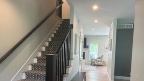 Eine moderne Treppe mit gemustertem Teppich und Holzstufen, die in einen Flur mit einer Bank und einem Sessel führt.