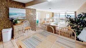 Ett rymligt vardagsrum med ett matbord, stolar, en soffa och ett stort fönster med utsikt över havet.
