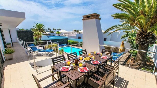 Area piscina sul tetto con tavolo da pranzo per quattro persone, circondata da poltrone relax e una palma.