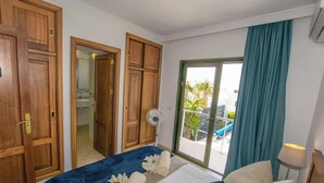 Una camera d'hotel con un letto, una ventola, vista all'esterno e porte in legno.