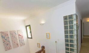 A hallway with white walls, a wooden staircase, and a glass block wall.