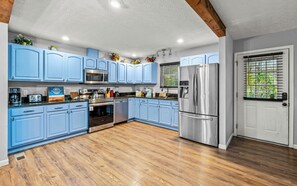 Kitchen features a refrigerator, oven, and microwave, with a wooden floor and exposed beams.