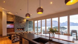 Una cucina moderna con parete in pietra, camino, ampia finestra vista montagna e luci a sospensione.