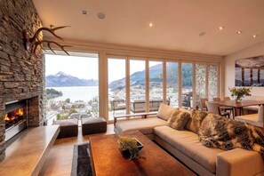 A modern living room with a stone fireplace, large windows, a sofa, and a dining area.