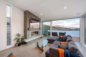 Un salon moderne avec une cheminée en pierre, une table basse en verre, un canapé et une vue sur un paysage montagneux grâce à de grandes fenêtres.