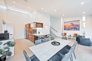 Un vaste espace de vie comprenant un coin repas avec table, une cuisine moderne et une grande fenêtre offrant une vue sur les montagnes.