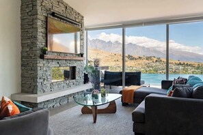 Un salon doté d’une cheminée en pierre, d’une table basse en verre et offrant une vue sur les montagnes et un lac.