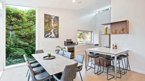 A modern kitchen with a dining area, large windows, and a view of greenery. - Toroa Chalet| Hot Tub, Gas Fire, BBQ, Free Parking (Queenstown)