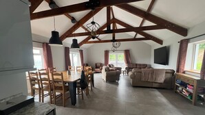 A spacious living area with a high ceiling and exposed wooden beams, a dining area with wooden furniture, and a sofa set. - Luxury Accessible Holiday Home with Hot Tub & Views (Llansawel)