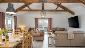A spacious living area with a wooden ceiling, a dining table set with plates and glasses, a sofa, and a television mounted on the wall. - Luxury Accessible Holiday Home with Hot Tub & Views (Llansawel)