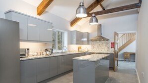 A modern kitchen with grey cabinets, a central island, pendant lighting, and a wooden staircase. - Luxury Accessible Holiday Home with Hot Tub & Views (Llansawel)