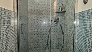 A glass-enclosed shower with a tiled wall, a handheld showerhead, and a handheld shower hose. - Augustus Room (Roma)