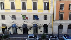 A building with multiple windows, some with shutters, and a flag with a red rose and a blue flag with yellow stars. - Augustus Room (Roma)