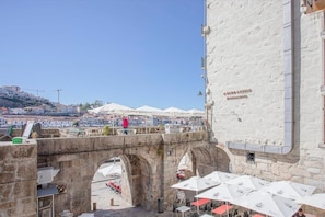 Un pont en pierre avec des arches, des tables à l’extérieur protégées par des parasols, et un bâtiment sur lequel on peut lire l’inscription « Restaurant OMMA ANTIAGO ».