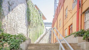 En trappa av sten med ett metallräcke, omgiven av byggnader – på ena sidan en byggnad med en stenmur och på den andra en röd byggnad.