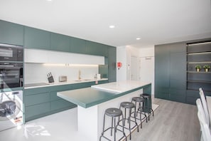 Une cuisine moderne avec des meubles de couleur turquoise, un îlot central doté de tabourets et des appareils électroménagers intégrés.