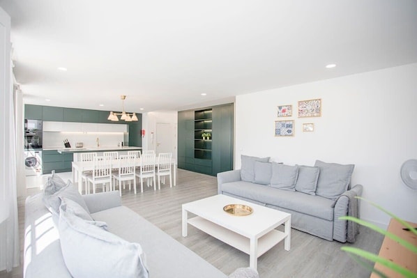Un salon moderne avec un canapé gris, une table basse blanche et un coin repas avec des chaises blanches.
