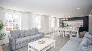 Ett modernt vardagsrum med en grå soffa, ett vitt soffbord och en matplats med vita stolar.