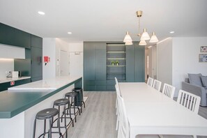 Une cuisine moderne avec un plan de travail blanc, des tabourets de bar et un coin repas comprenant une longue table et des chaises.