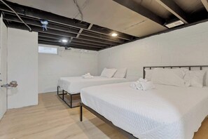 Una habitación con dos camas, ropa de cama blanca, suelo de madera y pared de ladrillo blanco.