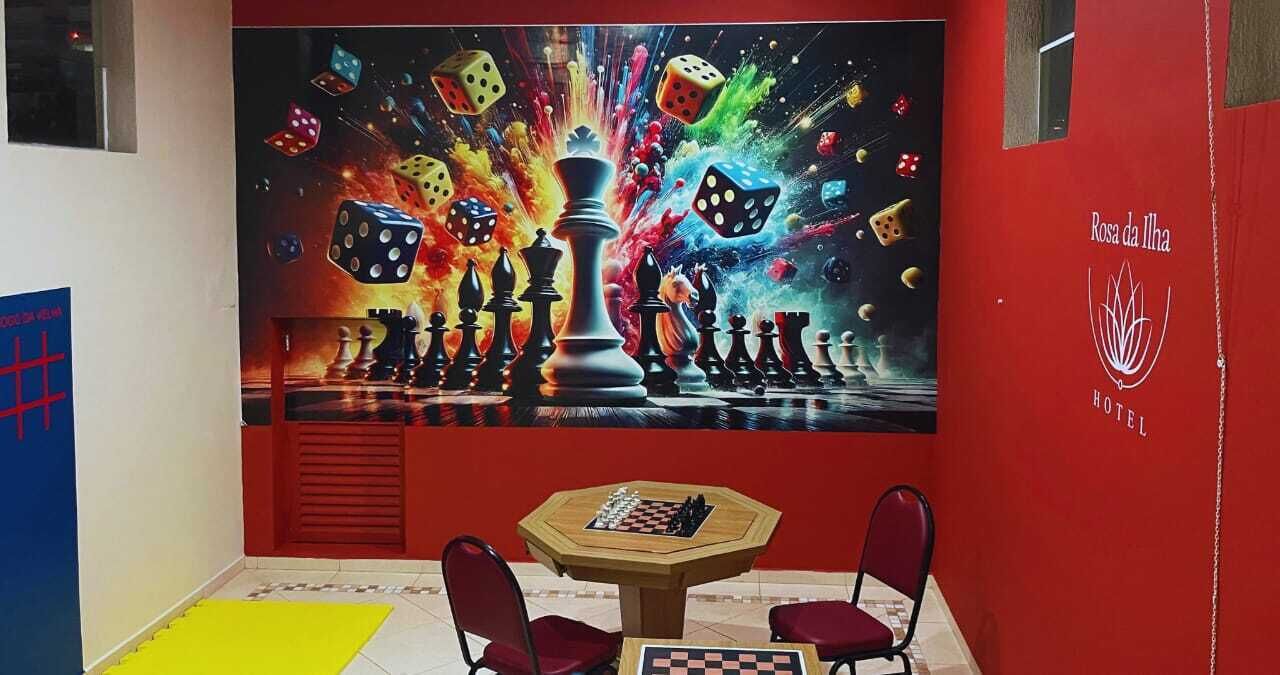 A room with a chessboard, a painting of dice and chess pieces, and a red wall with the hotel name.
