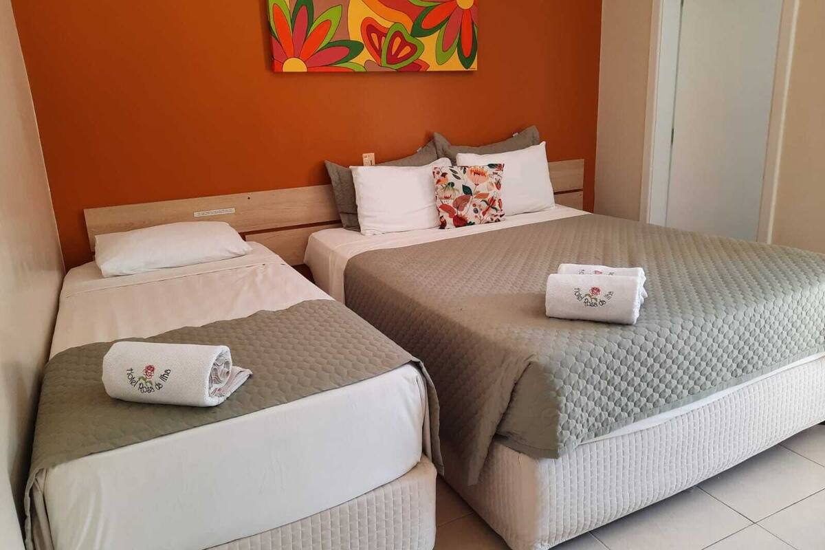 A hotel room with two beds, each with a pillow and a folded towel. There is a colorful painting on the wall above the beds.