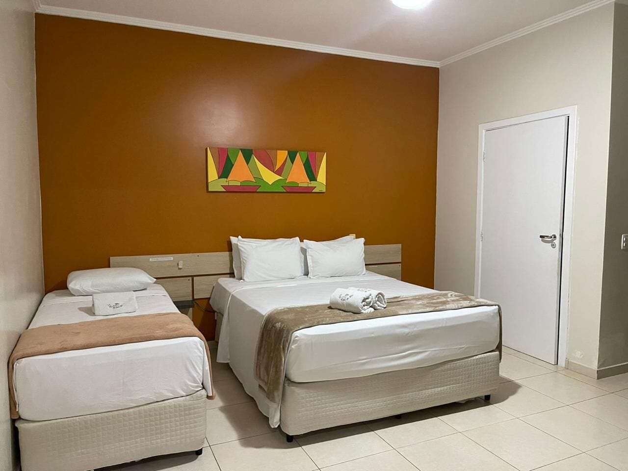 A hotel room with a bed, a smaller bed, a wardrobe, and a painting on the wall.