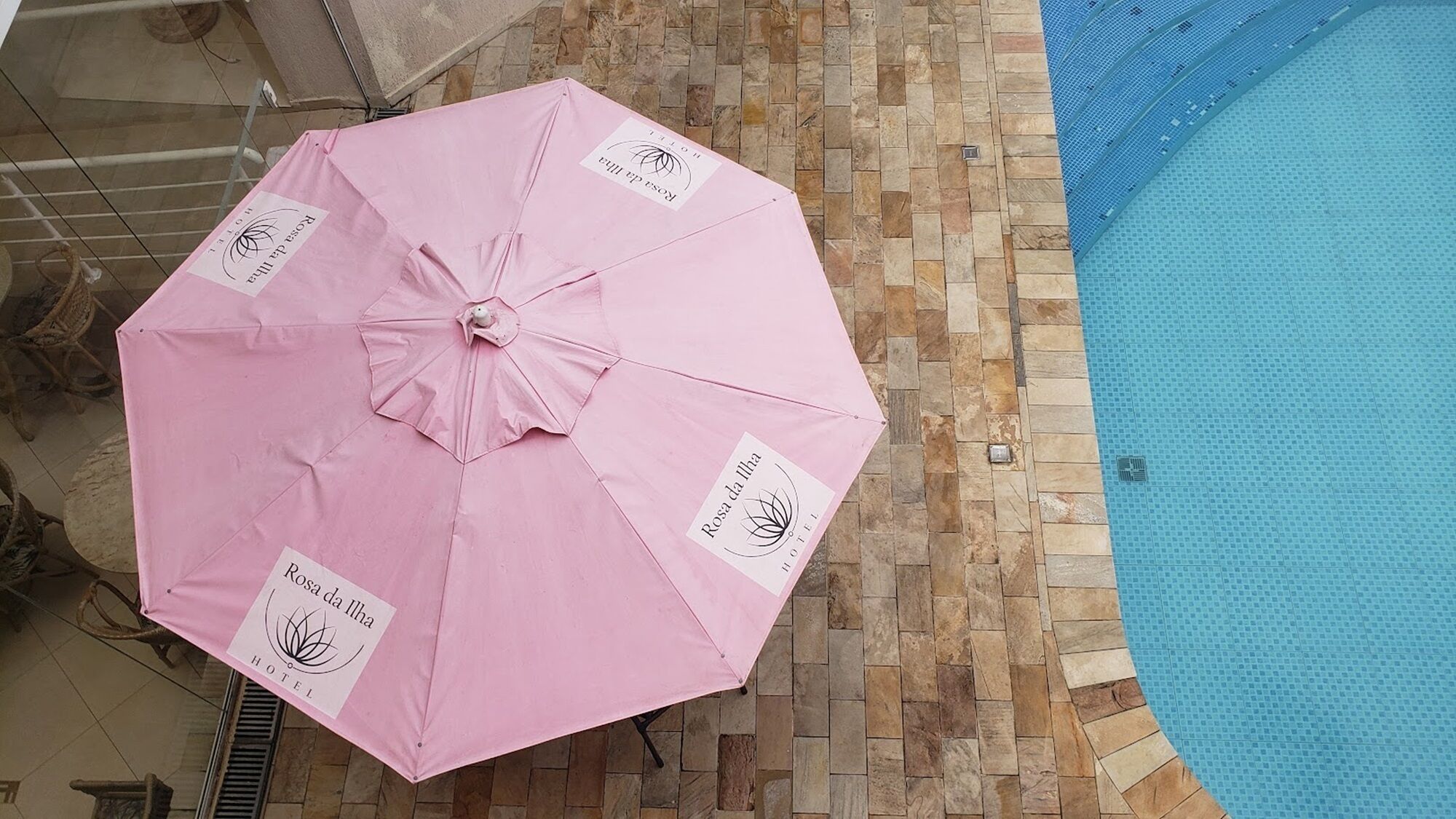 Ein pinker Schirm mit Hotel-Logo, platziert auf einer gefliesten Terrasse in der Nähe eines Schwimmbeckens.