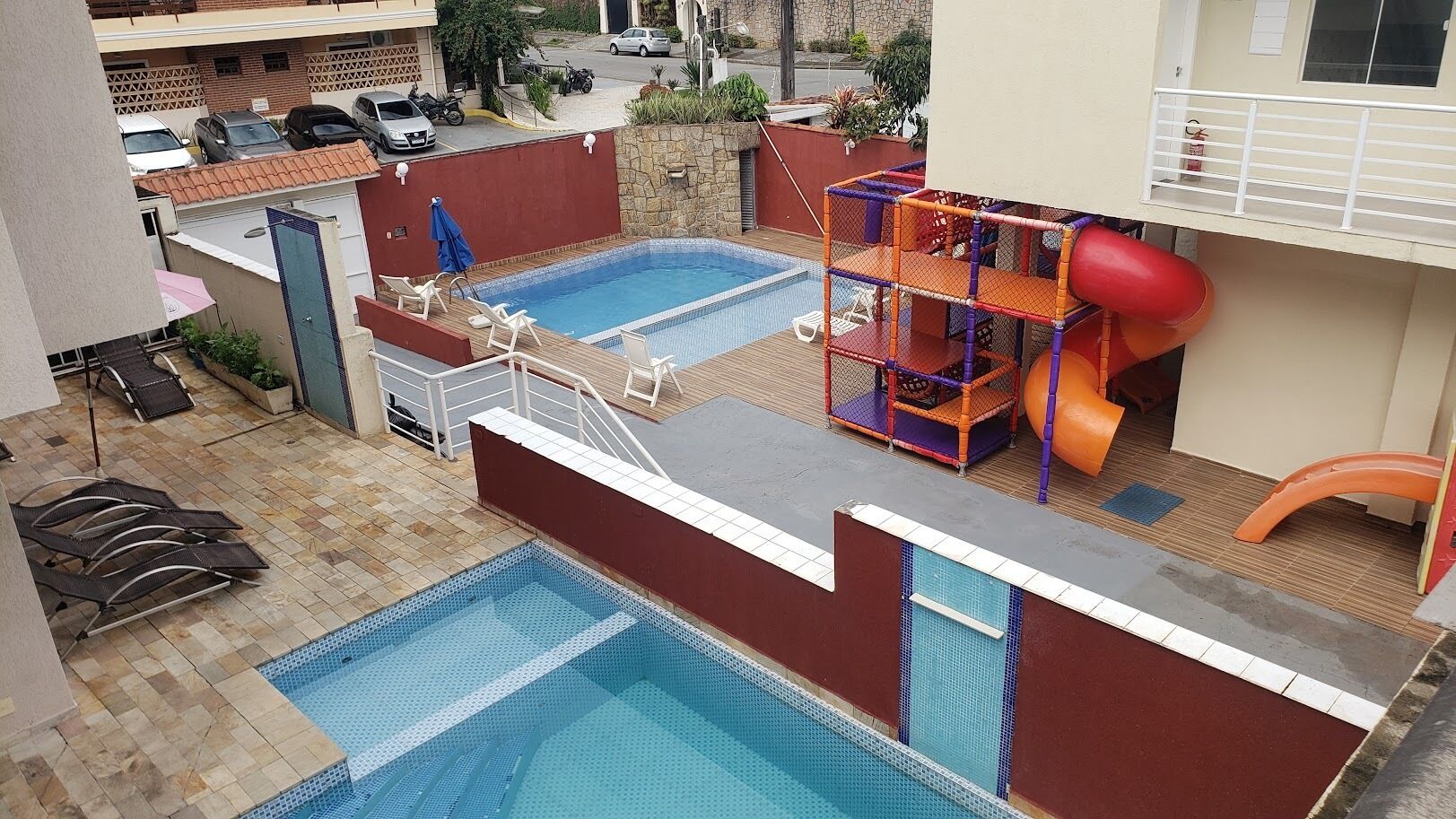 Un área de piscina con dos piscinas, un tobogán y sillas de descanso.