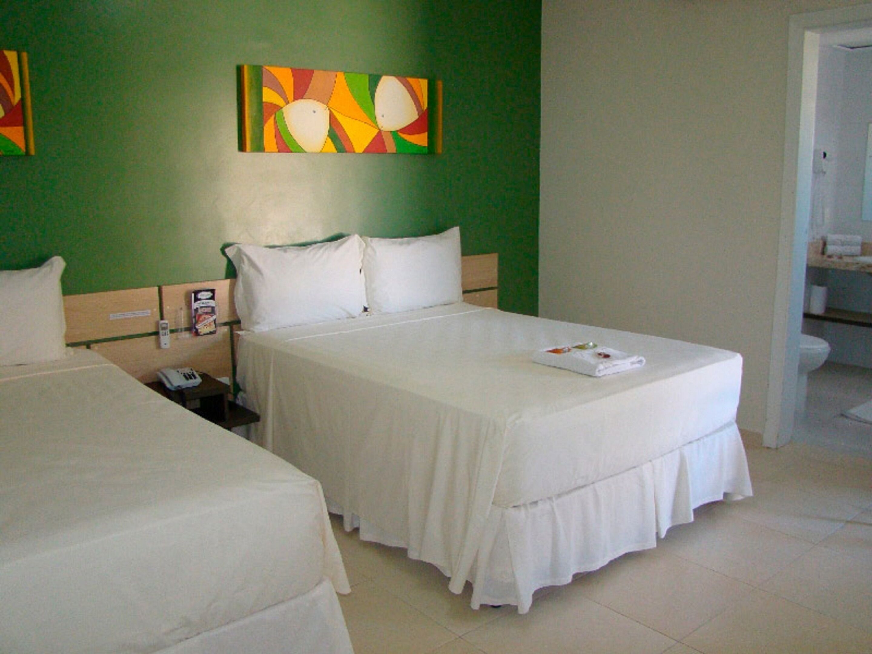 Une chambre d’hôtel avec deux lits, un mur vert et un tableau.
