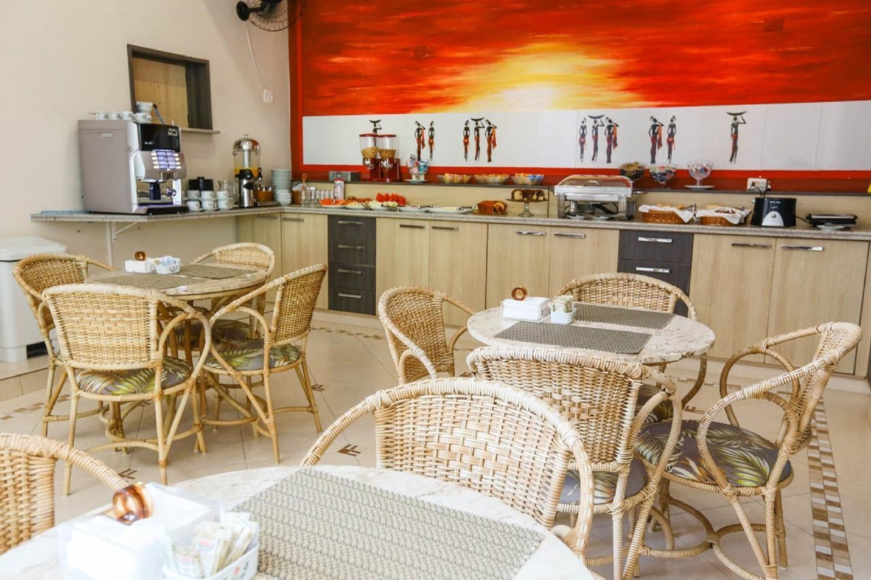 Een restaurant met rieten meubels, een koffieapparaat en een grote rode muurschildering.