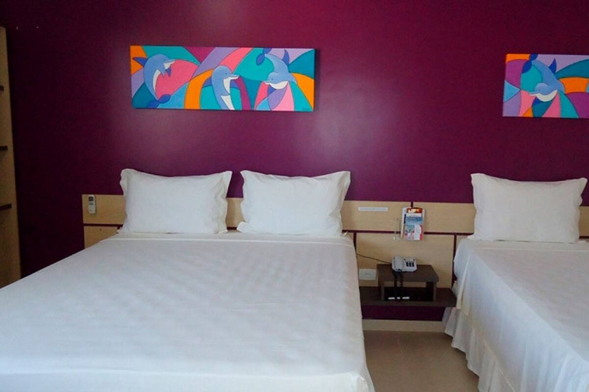 A hotel room with two beds, white bedding, and purple walls. There are two paintings on the wall.