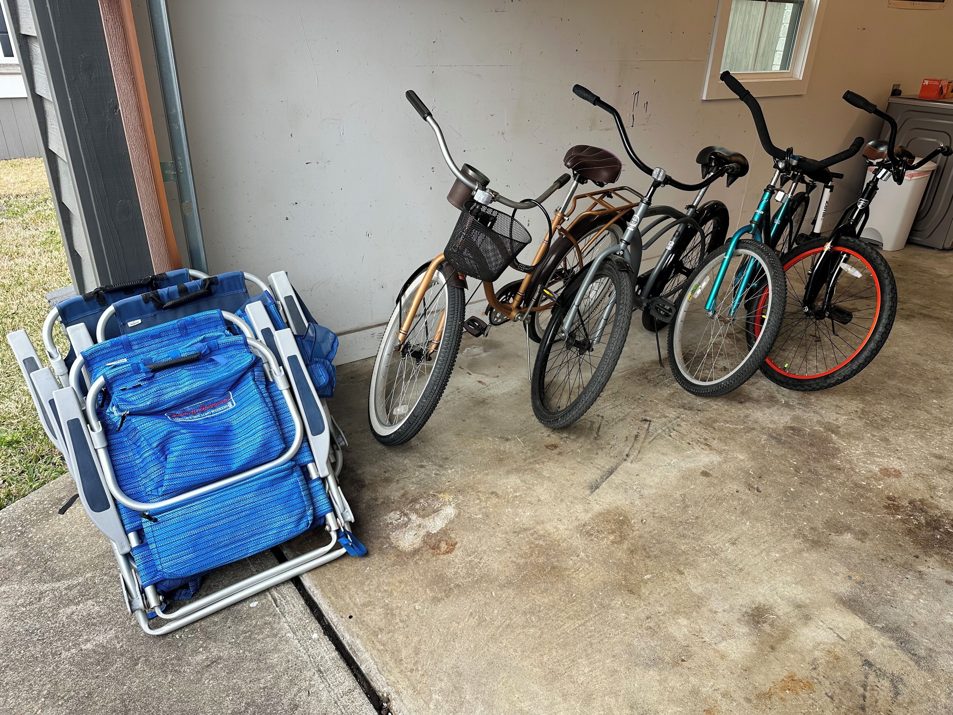 A bicycle rack with three bicycles and a blue luggage cart outside a building.