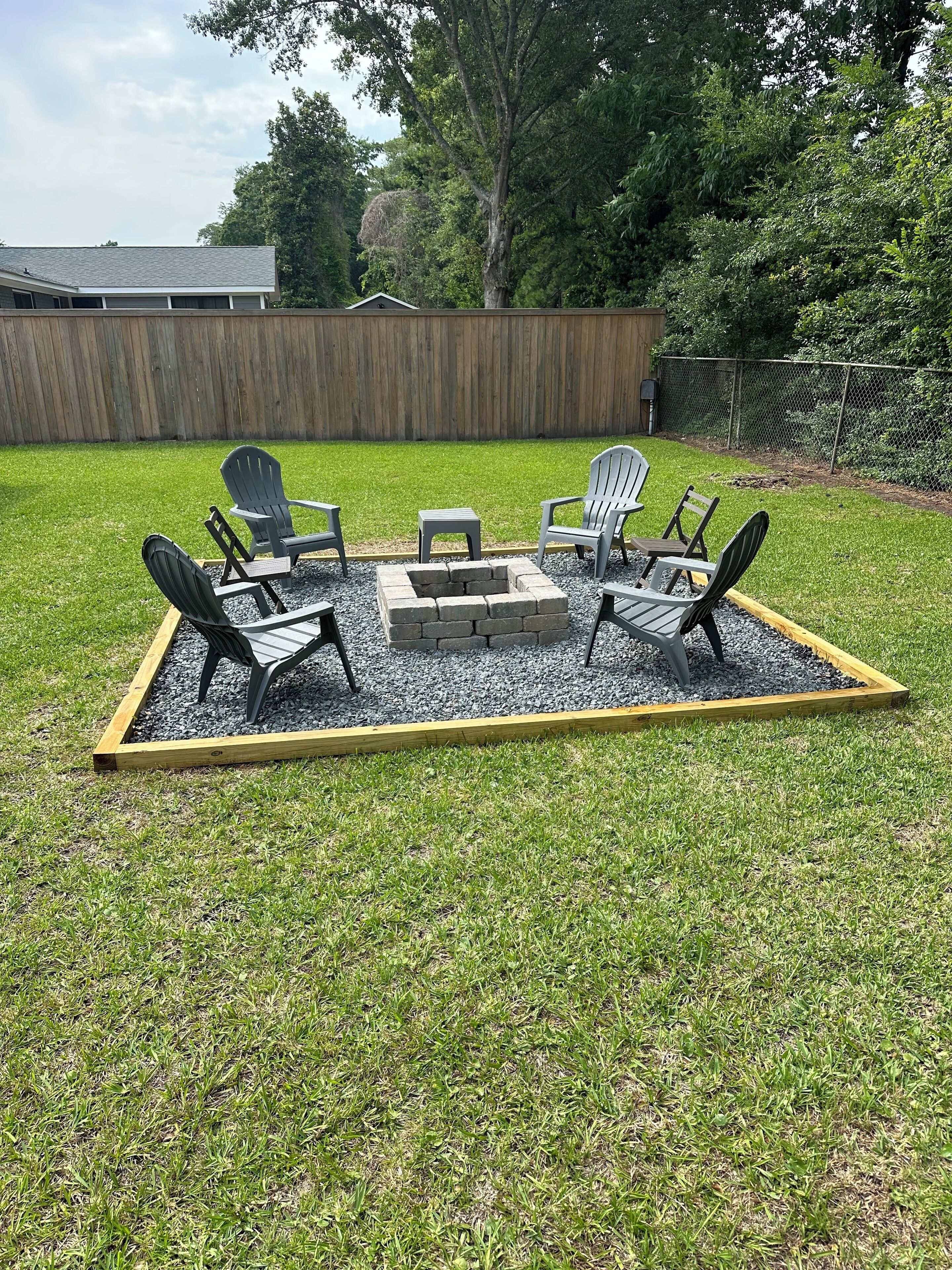 Een achtertuin met een vuurplaats, vier Adirondack stoelen en een houten terras.