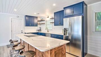 A modern kitchen with blue cabinets, a large island with stools, and a stainless steel refrigerator.