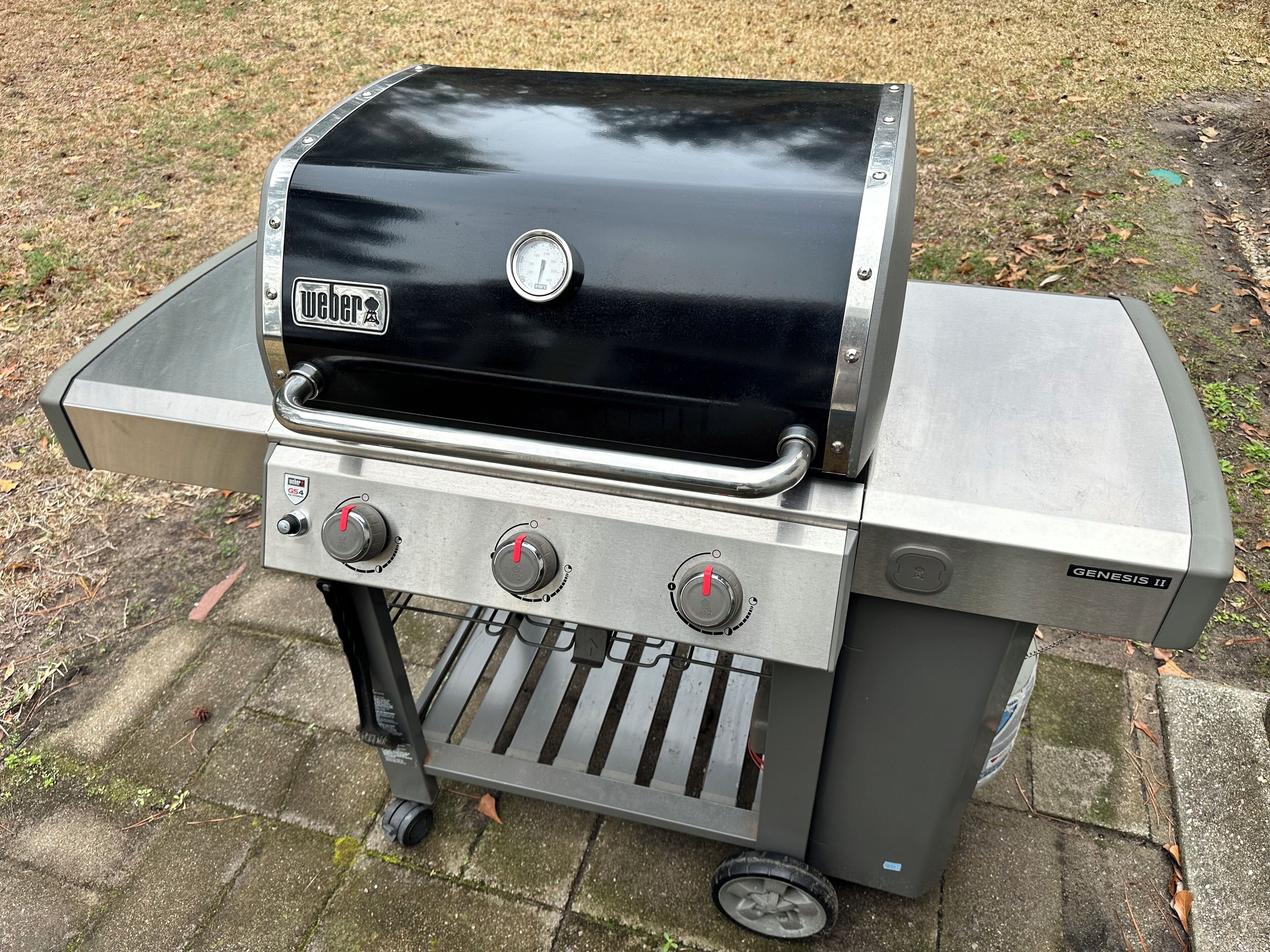 A portable Weber Genesis II grill with four control knobs and a digital thermometer.