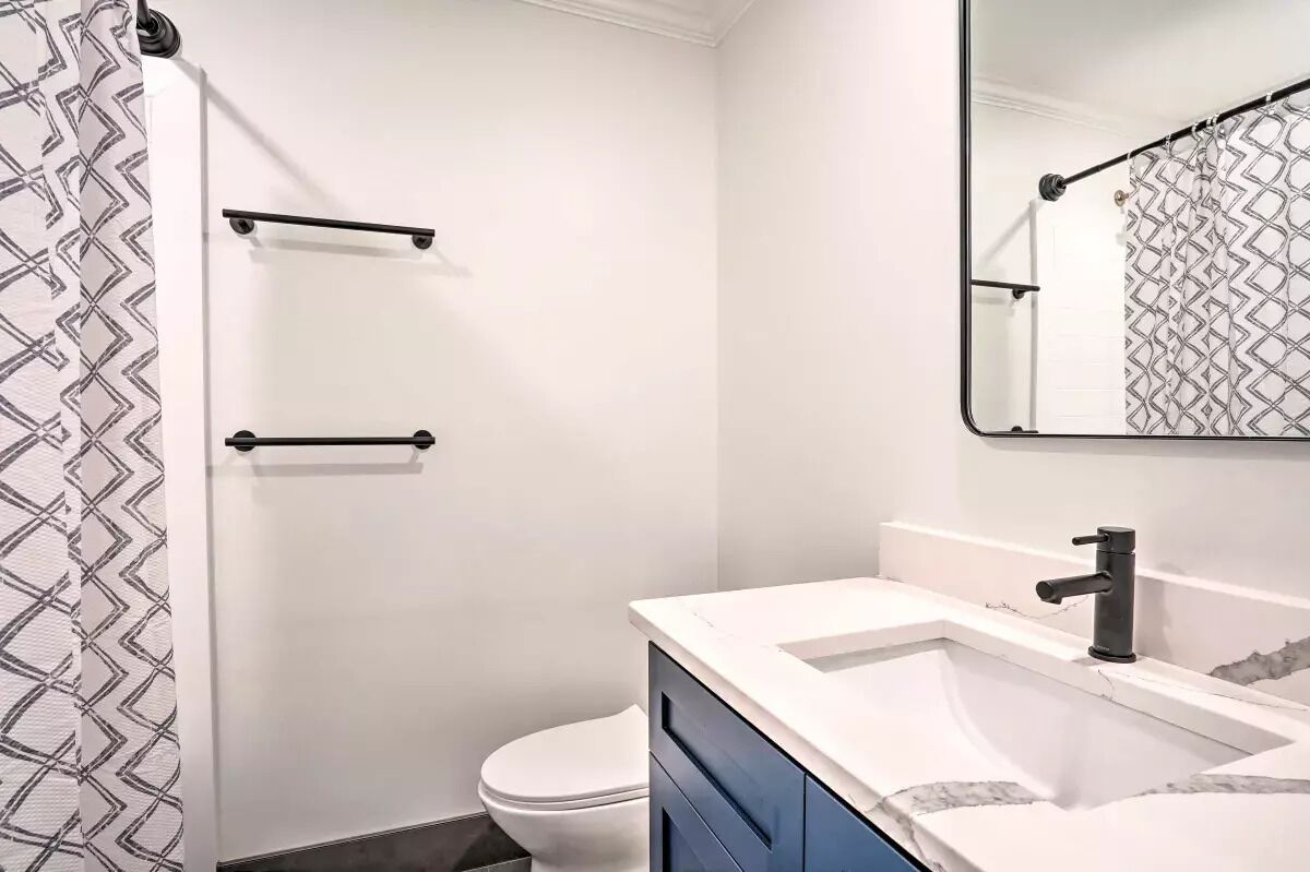 A modern bathroom with a white toilet, a sink with a marble countertop, and a shower curtain with a geometric pattern.