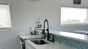 Cozinha moderna com bancada branca, pia de aço inoxidável e backsplash com azulejos verde-água.