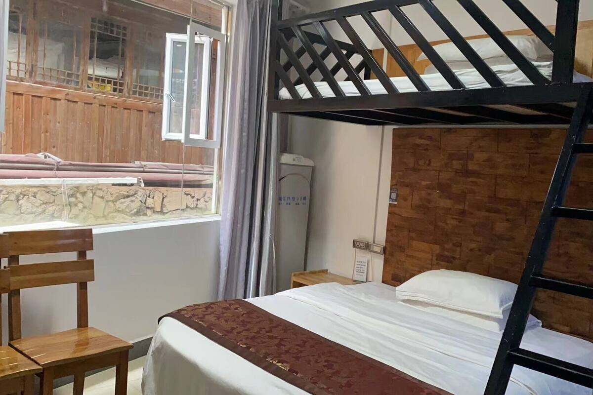 Een slaapkamer met een stapelbed, een houten trap, een bureau en een raam dat uitkijkt op een bouwplaats.