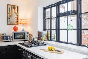 Una cocina con estufa, microondas y ventana con vista a un edificio de ladrillo.