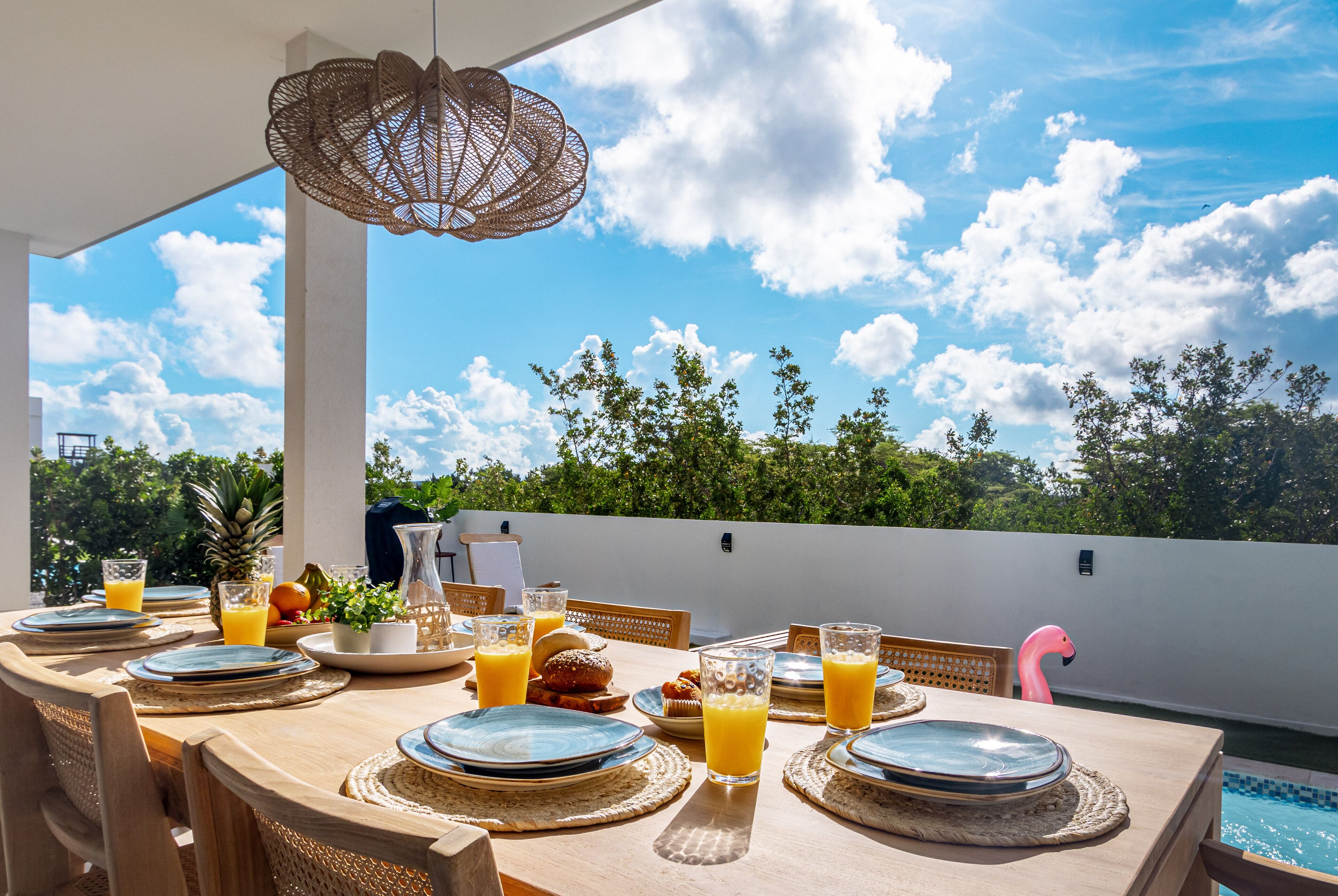 Un espacio al aire libre para comer con una mesa dispuesta para el desayuno, incluyendo platos, vasos y una decoración de flamenco.