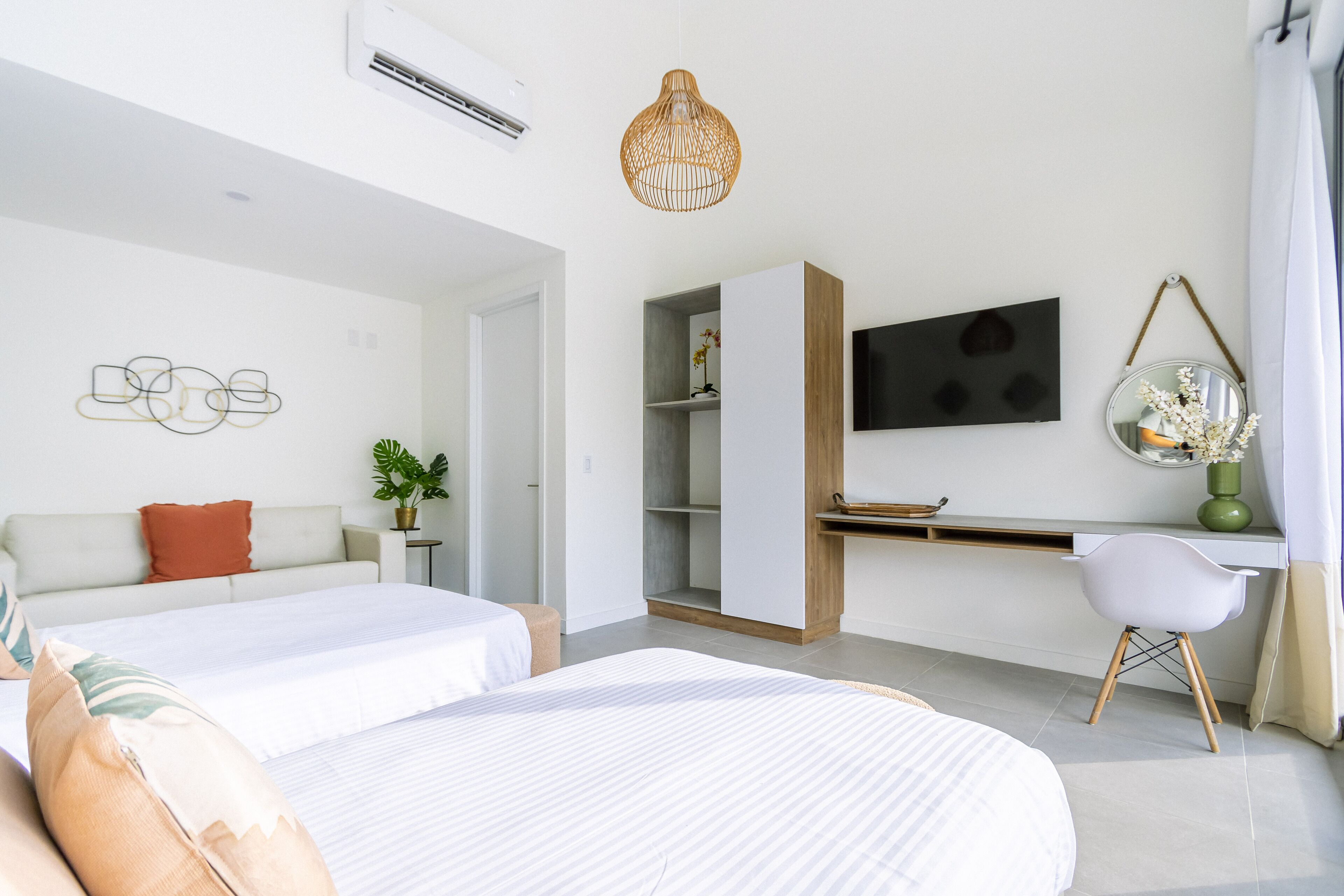 Quarto de hotel moderno com duas camas, uma escrivaninha, uma TV e um espelho suspenso.