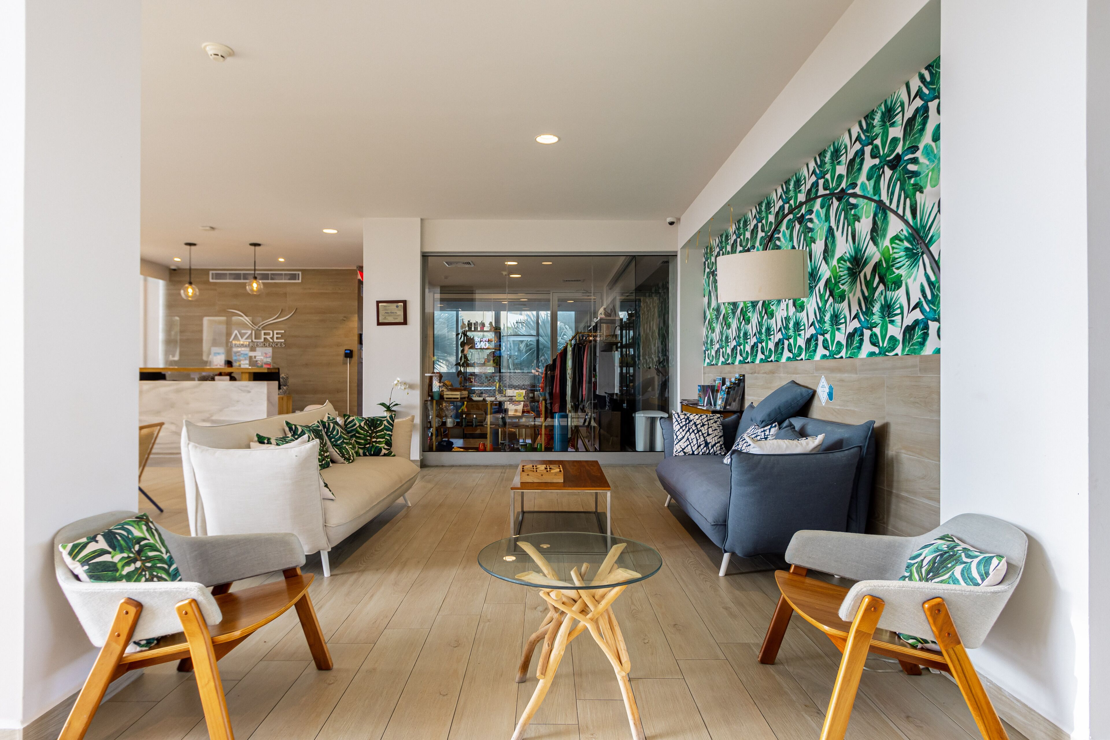A modern living room with a glass coffee table, two sofas, and a large tropical leaf-patterned wall.