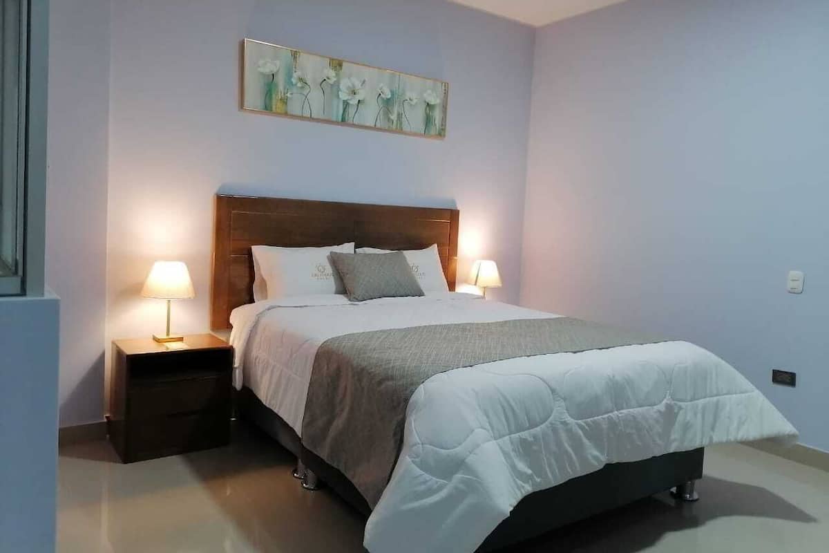 A bedroom with a bed, two bedside tables, a nightstand, and a wall-mounted painting.