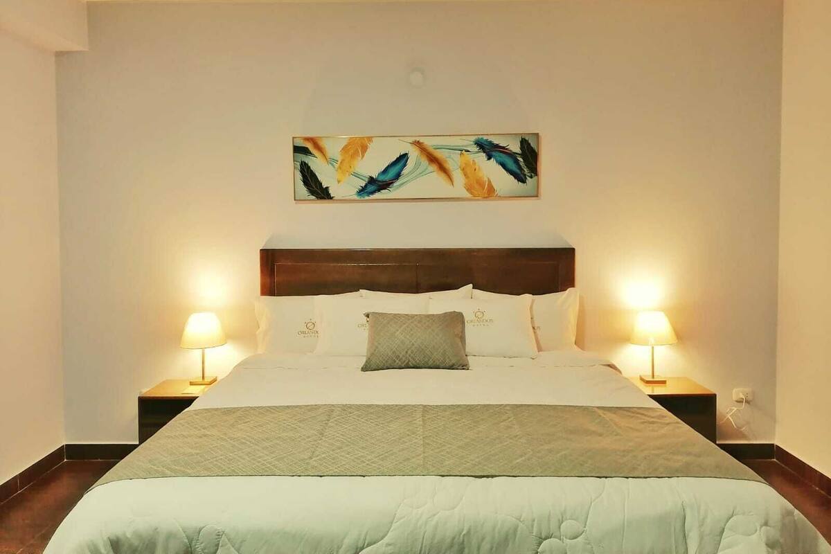 A neatly made bed with a wooden headboard, two bedside lamps, and a wall-mounted artwork above it.
