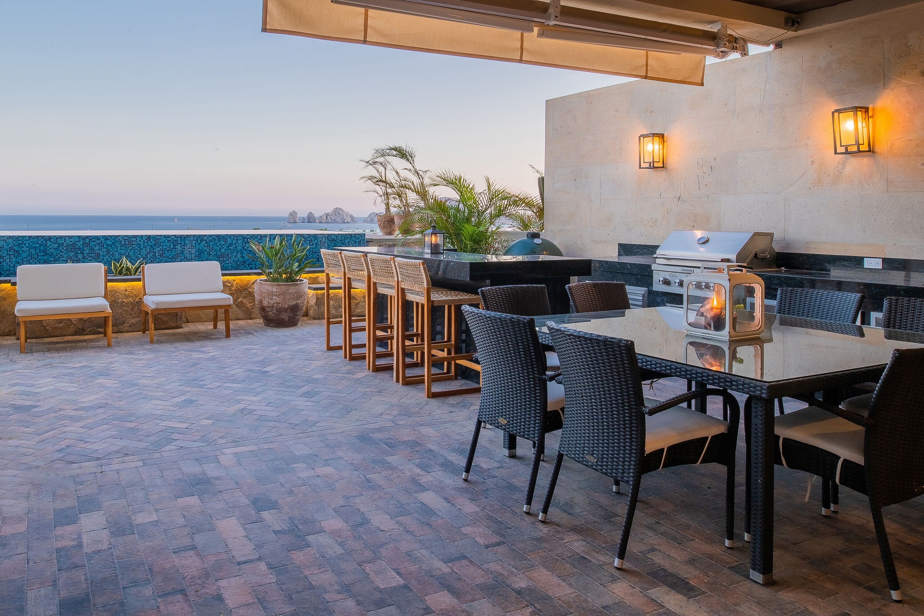 An outdoor patio with a grill, seating, and a view of the ocean.