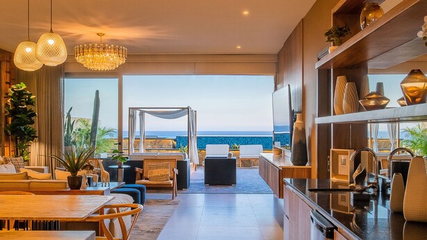 A modern interior with a dining area, seating, a view of the ocean, and a chandelier.