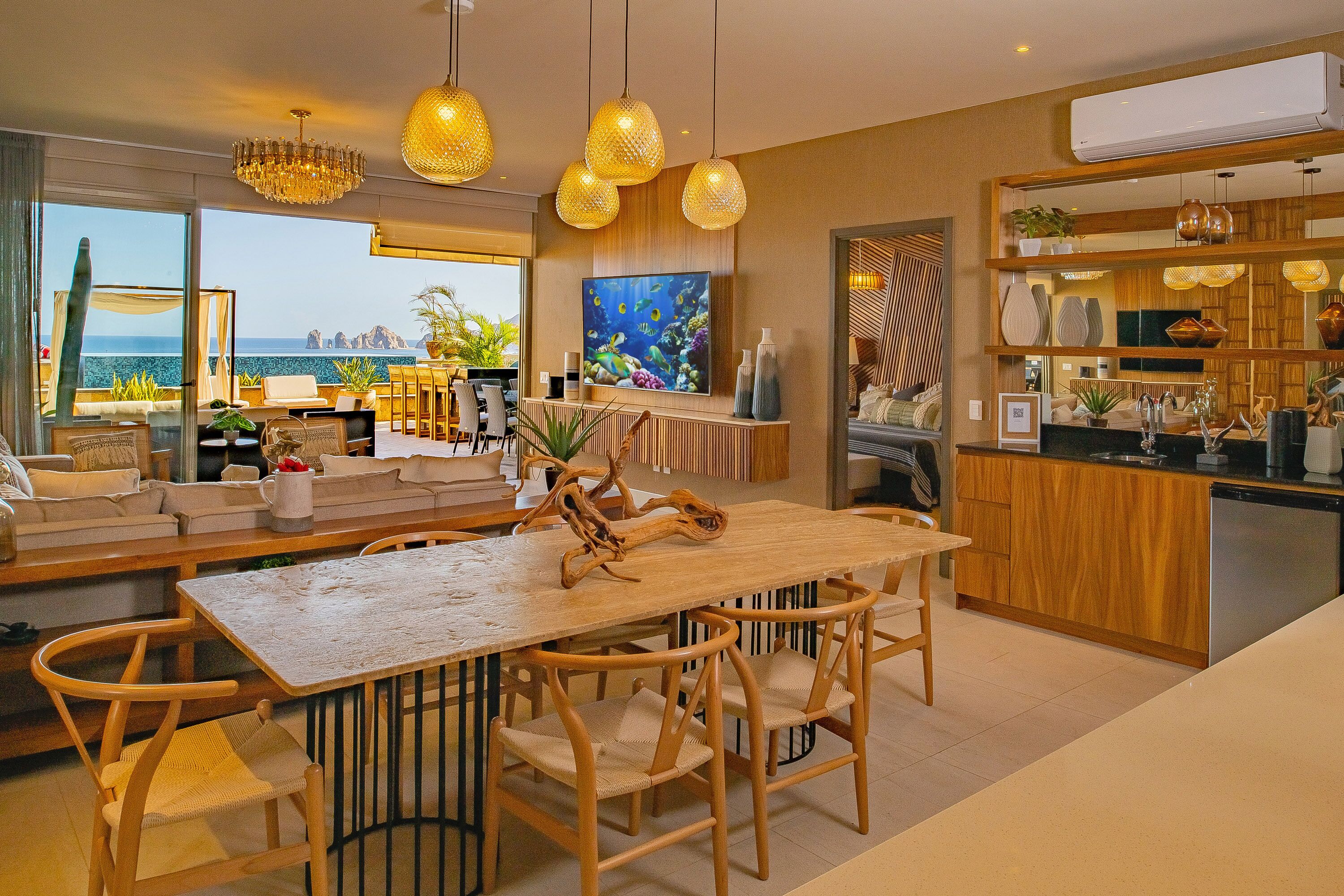 Een moderne keuken met houten aanrecht, een eethoek met een houten tafel en stoelen, en een groot raam met uitzicht op zee.